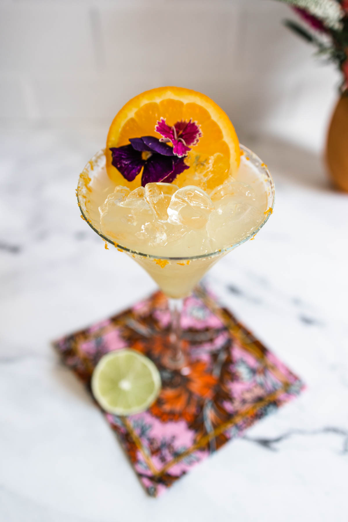 A close-up shot of Lillet margarita garnished with an orange slice and a red flower on top of a colorful napkin.