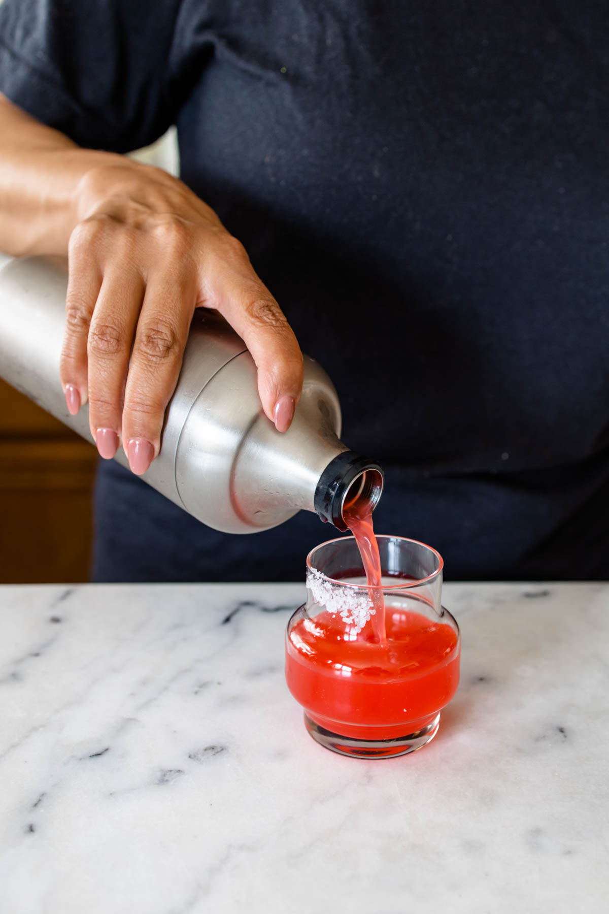 A person straining a Deadpool margarita mixture into a small glass with a salt rim.