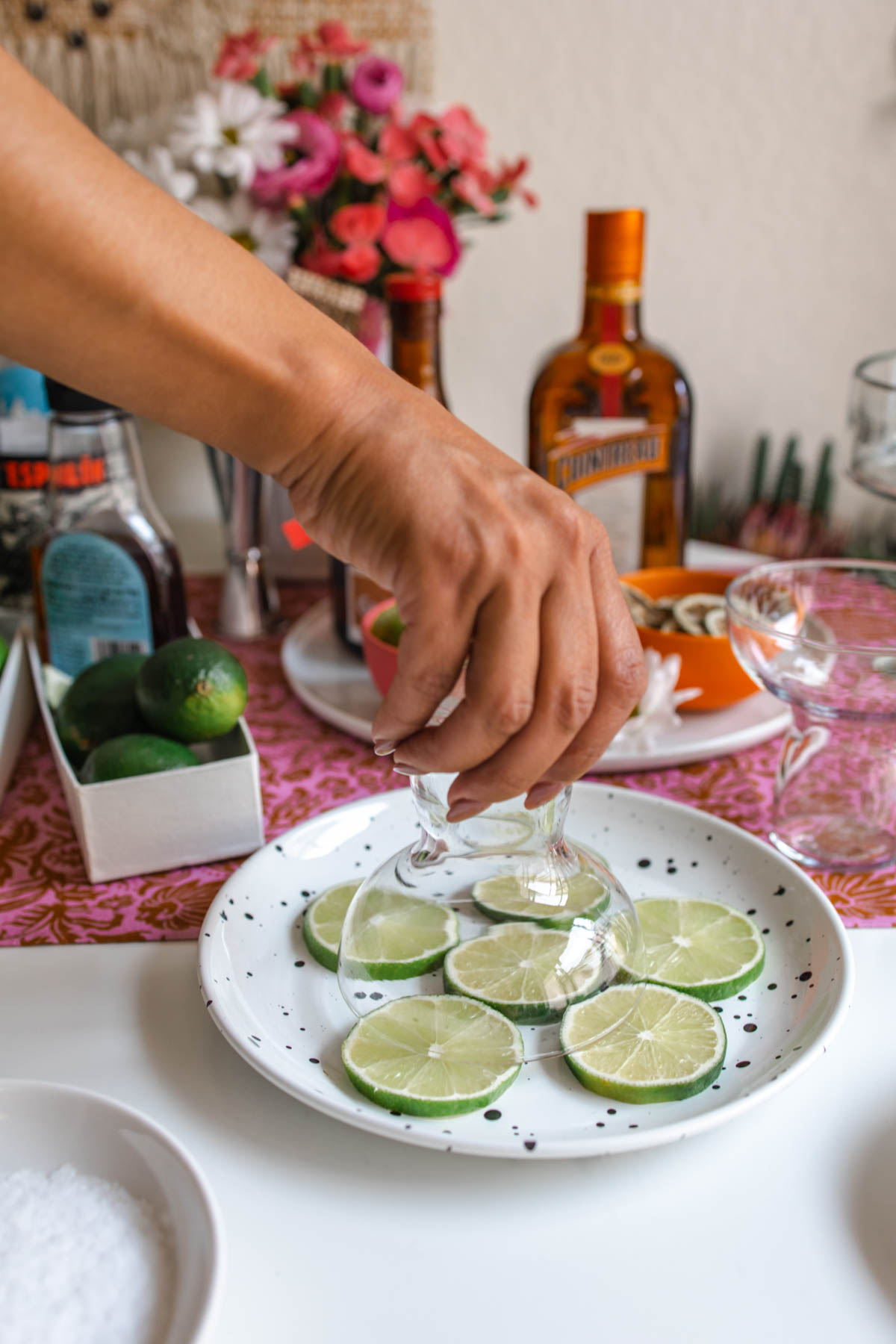 A person dipping their upside down margarita glass into a plate with sliced limes.