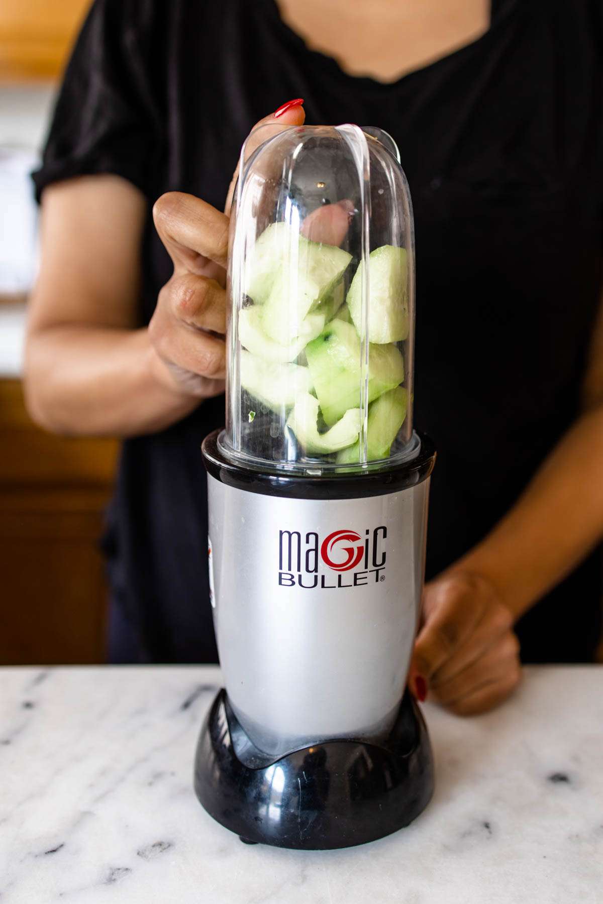 A woman holding the Magic Bullet blender with cucumber slices inside it.