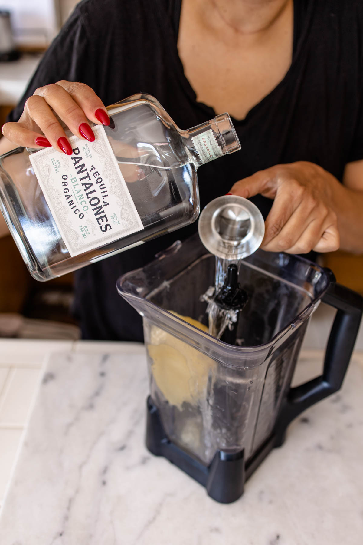 A person pouring some Pantalones Tequila Blanco from a jigger into a blender.