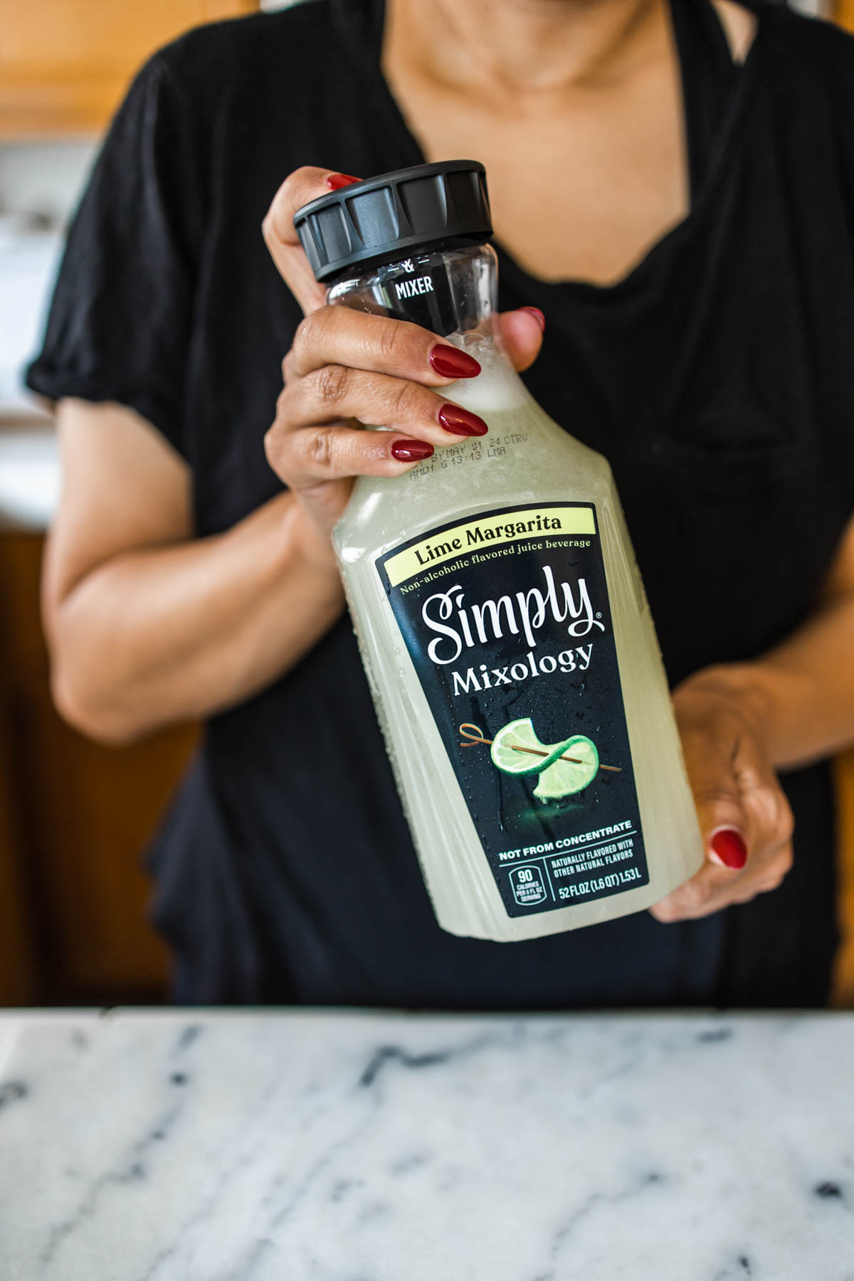 A woman in a black shirt holding a Simply Mixology bottle with both her hands.