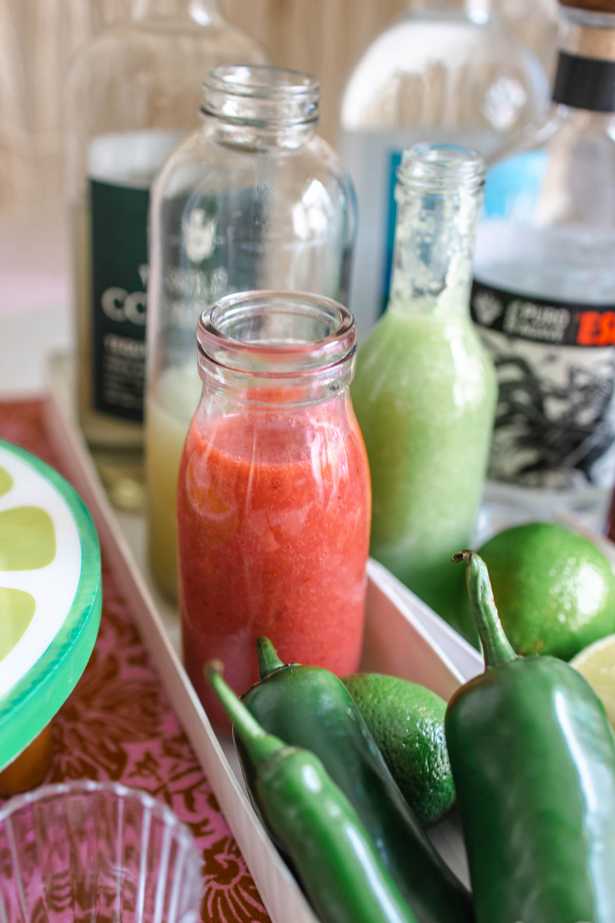 Whole jalapeno and serrano peppers in front of bottles of fruit juice and tequilas.