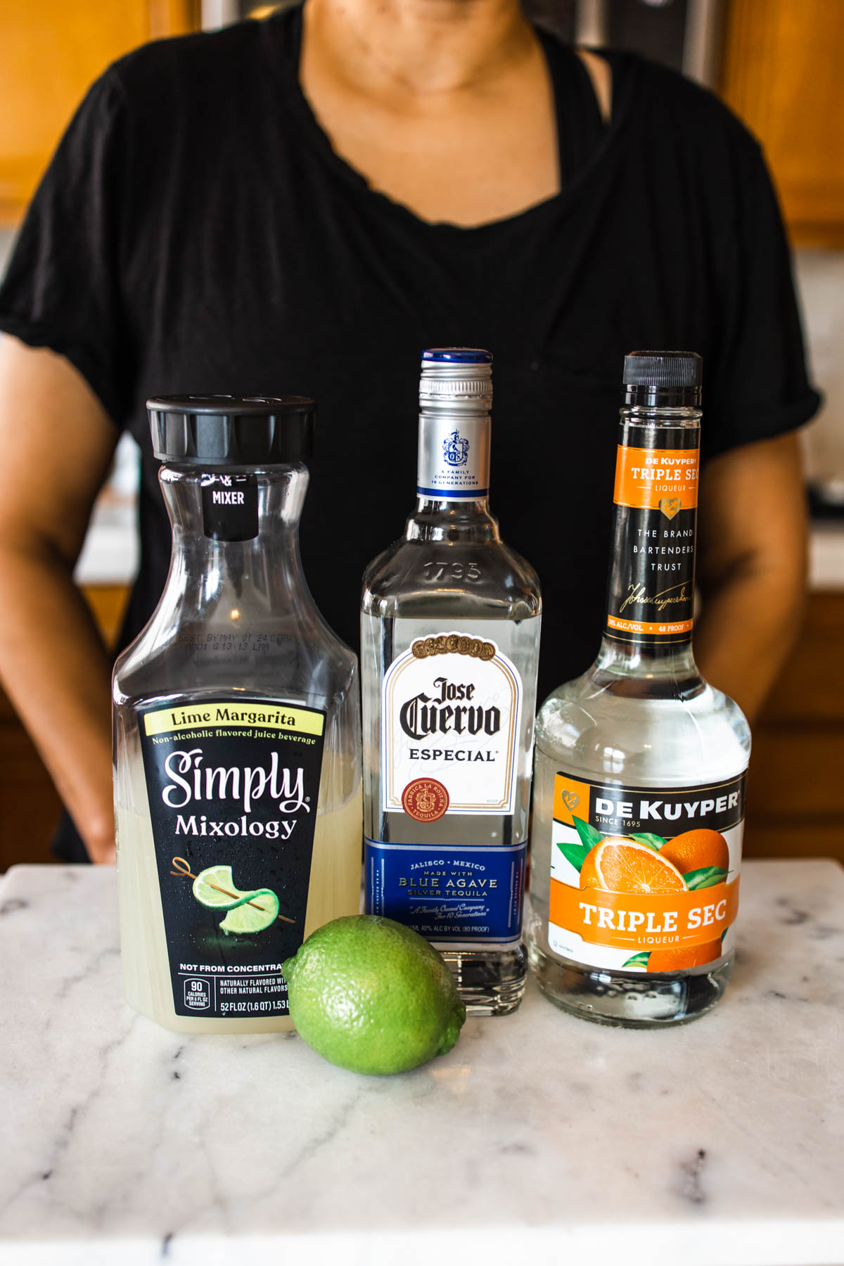 Bottles of Simply Mixology, Jose Cuervo Silver Tequila, Triple Sec, and a fresh lime on a counter.