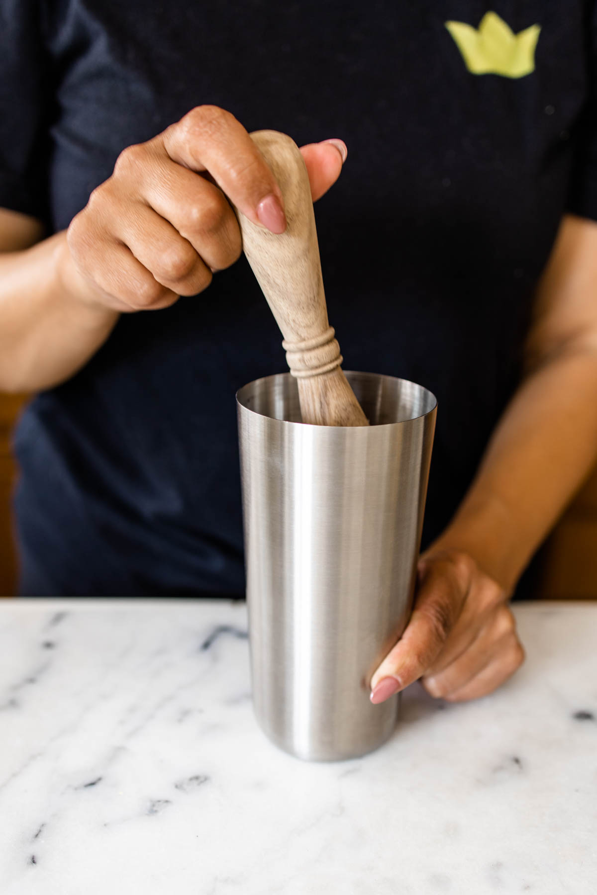 A person muddling ingredients inside a cocktail shaker.