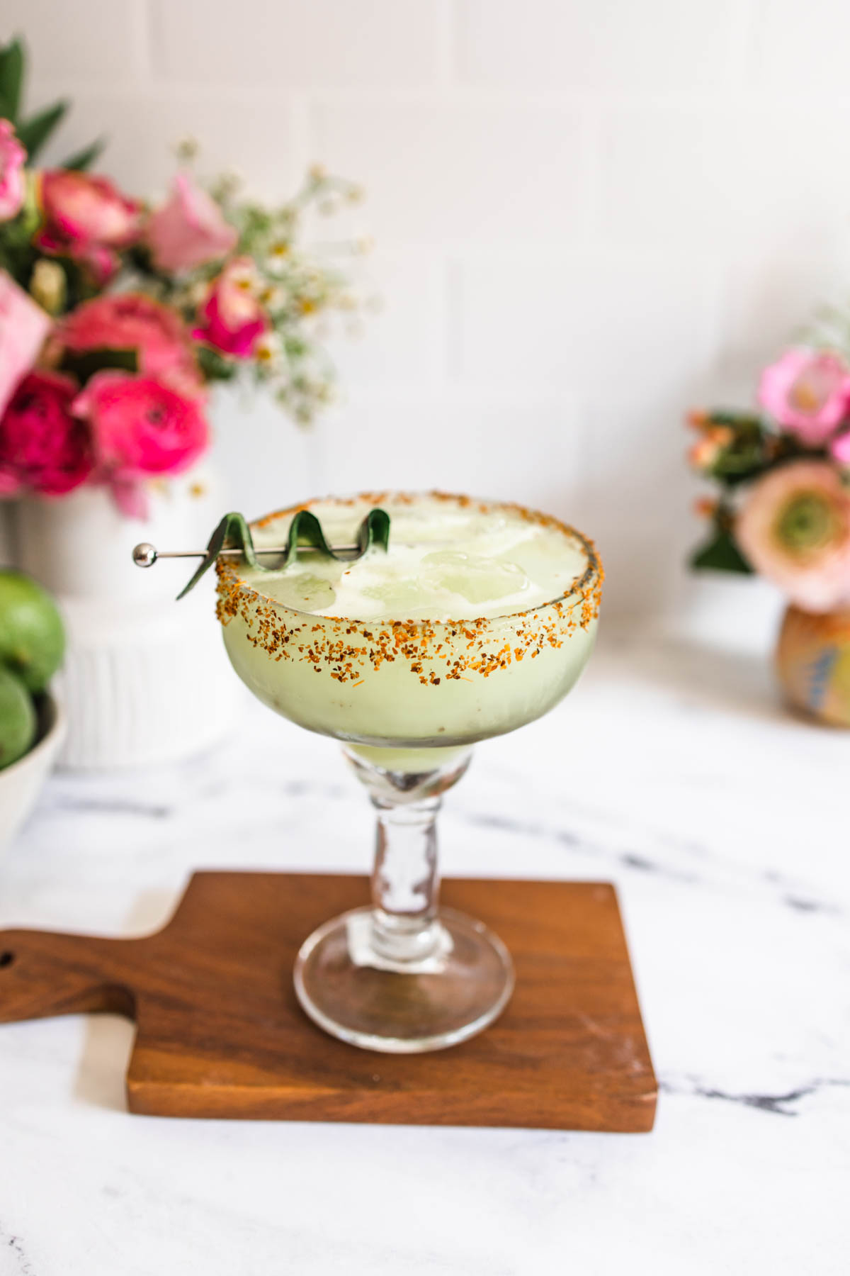 A cucumber margarita in a clear margarita glass with Tajin rim garnished with cucumber skin. 