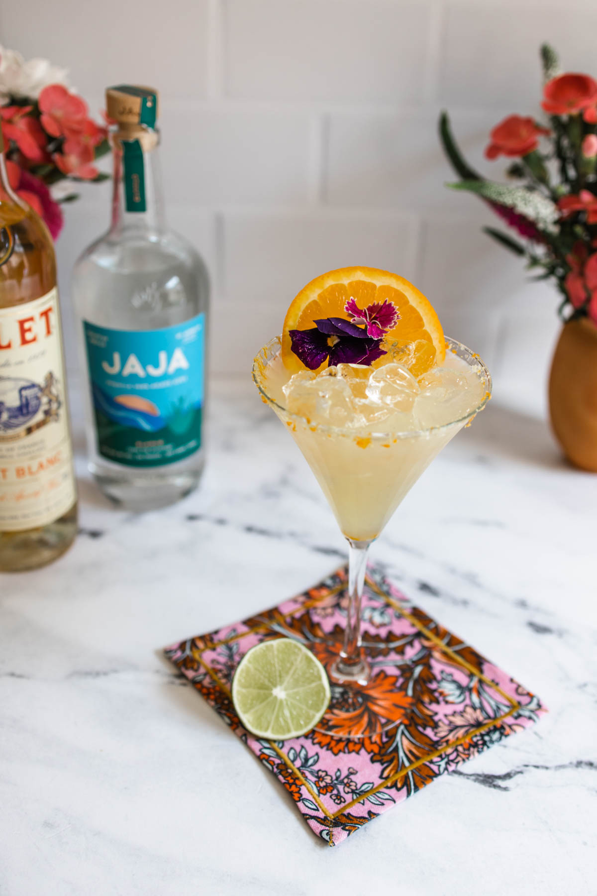 A Lillet Margarita in an orange salt-rimmed glass on top of a colorful napkin beside a slice of lime.