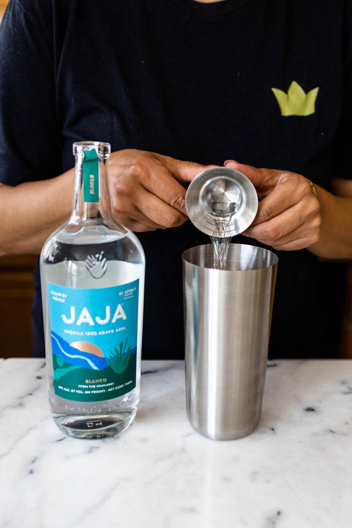 A person adding some JAJA Blanco Tequila from a jigger into a cocktail shaker.