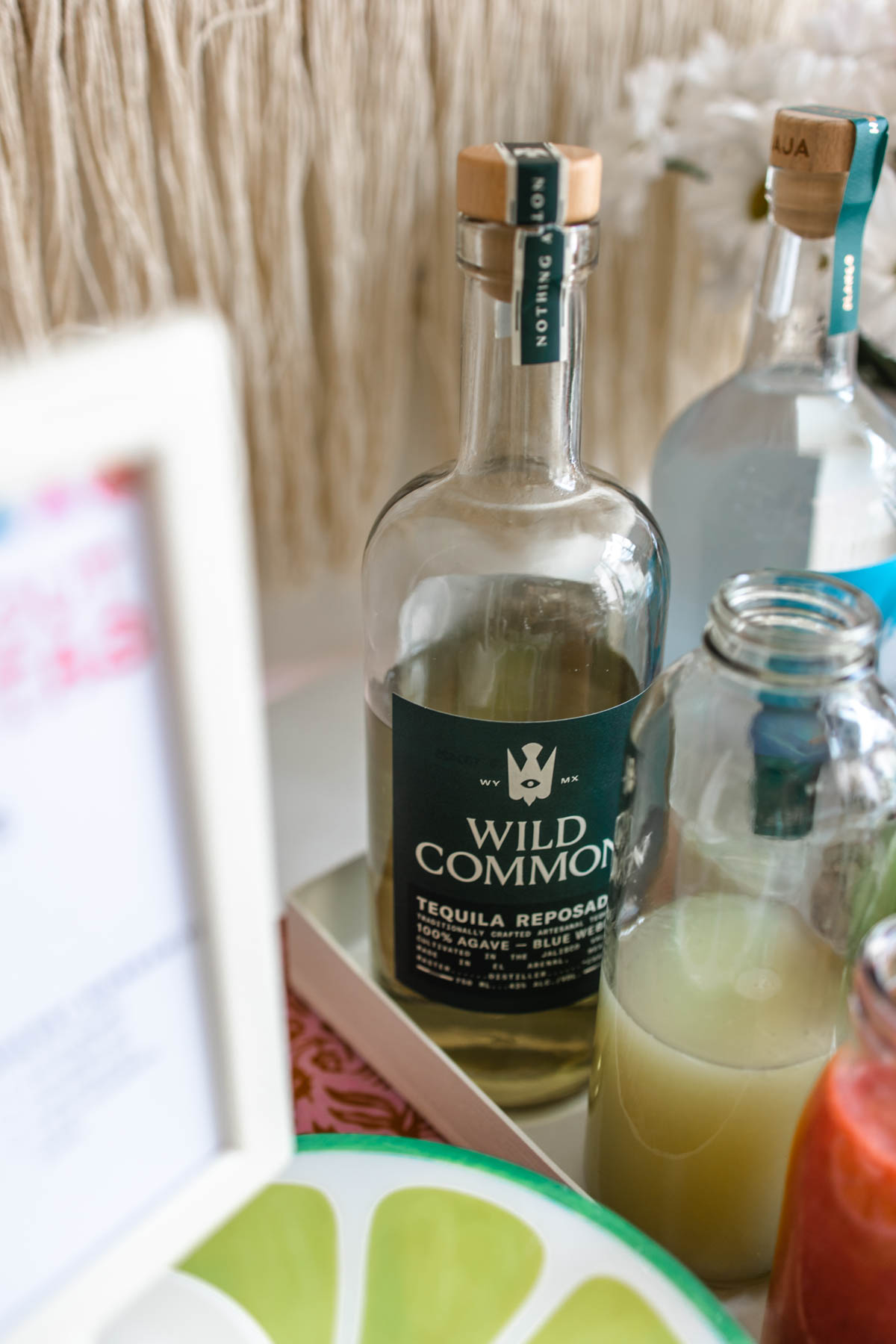 A bottle of Wild Common Tequila Reposado behind a bottle of fruit juice.