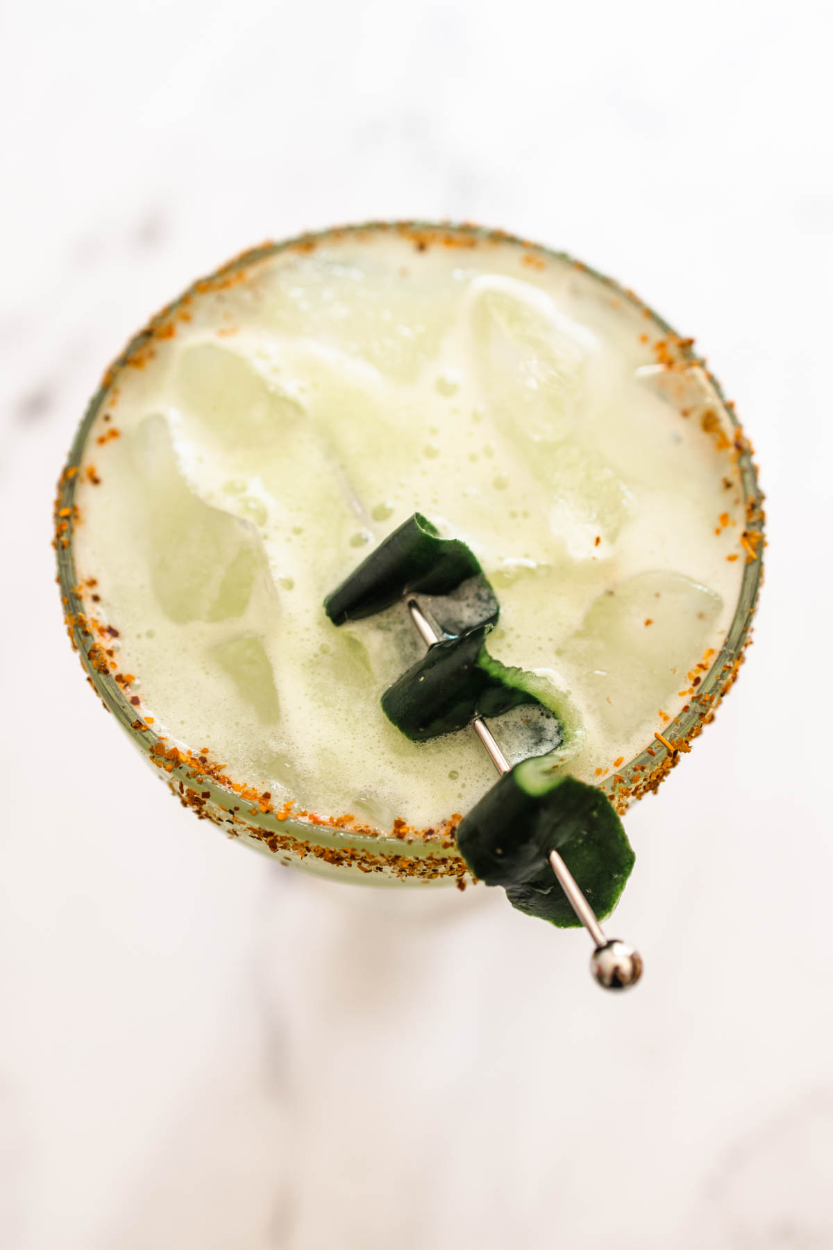 Top view of a delicious glass of cucumber margarita with ice and a Tajin rim garnished with skewered cucumber skin.