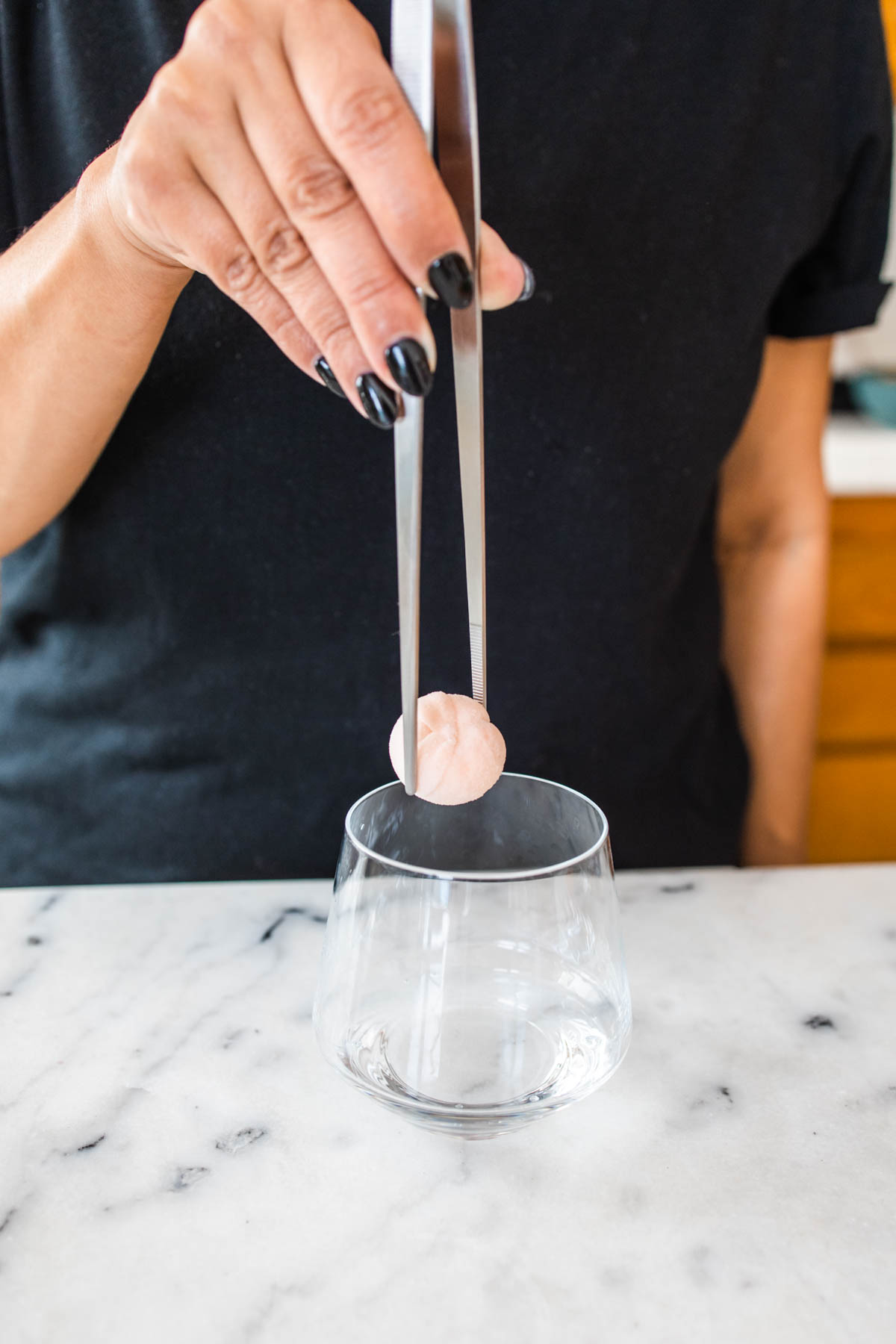 A person putting a drink bomb inside a glass using a kitchen tweezer.