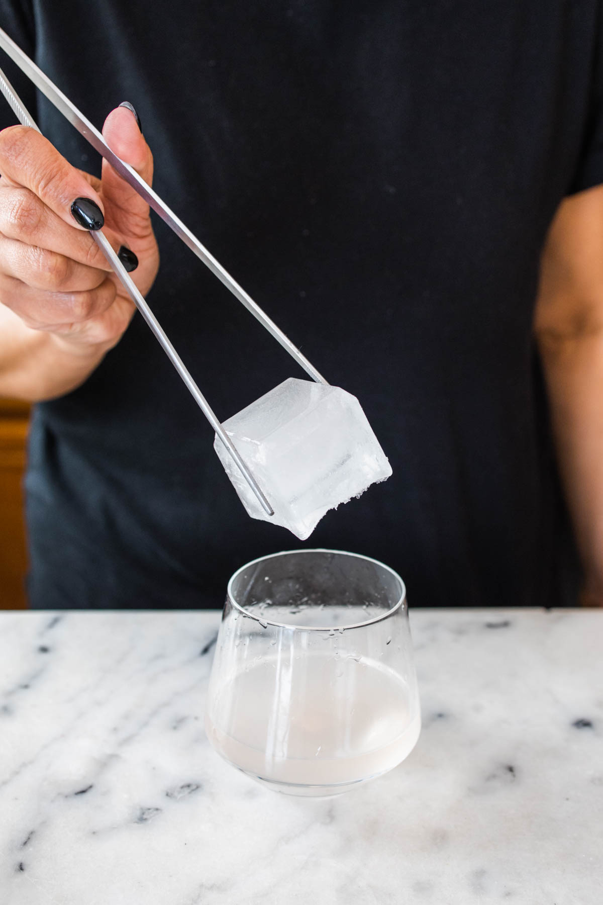 A person putting a large ice cube into a glass with peach margarita.