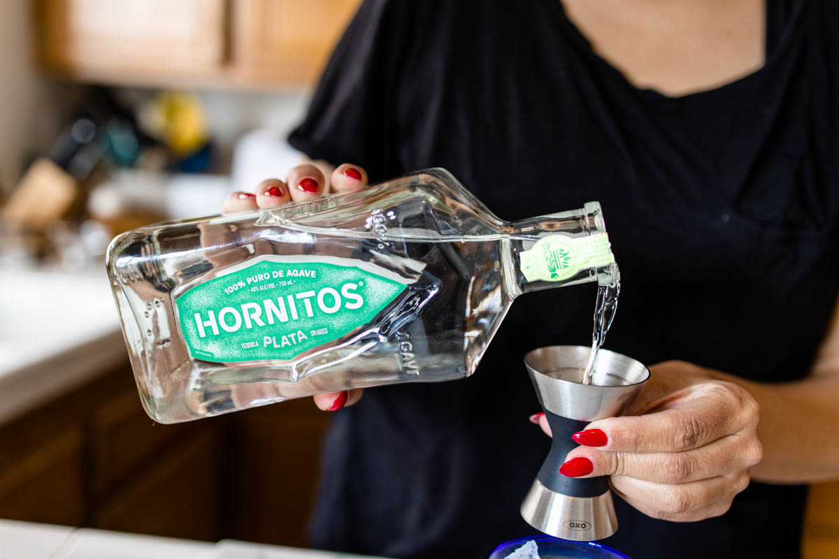 A person pouring some Hornitos Tequila Plata from its bottle into a jigger.