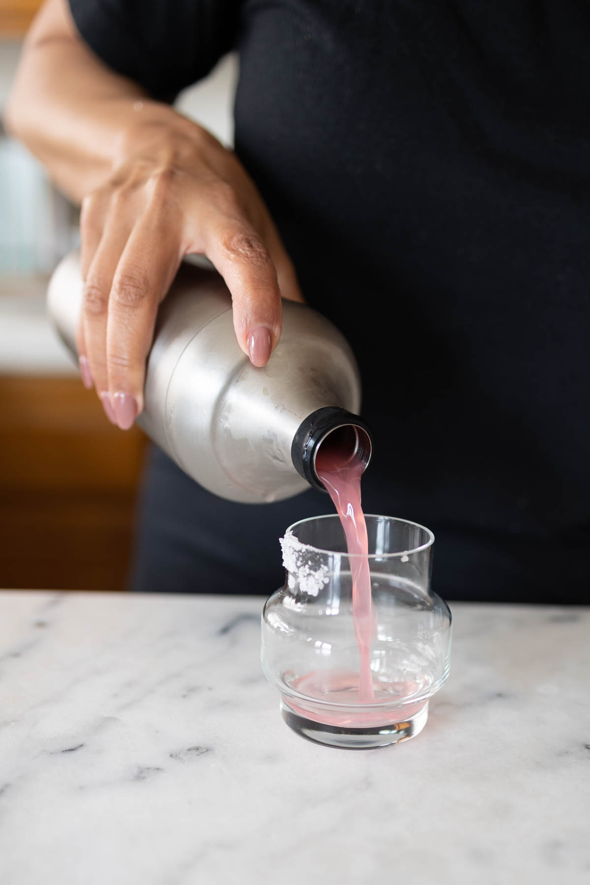 A person pouring a reddish Deadpool margarita into a taster-sized glass on top of a counter.