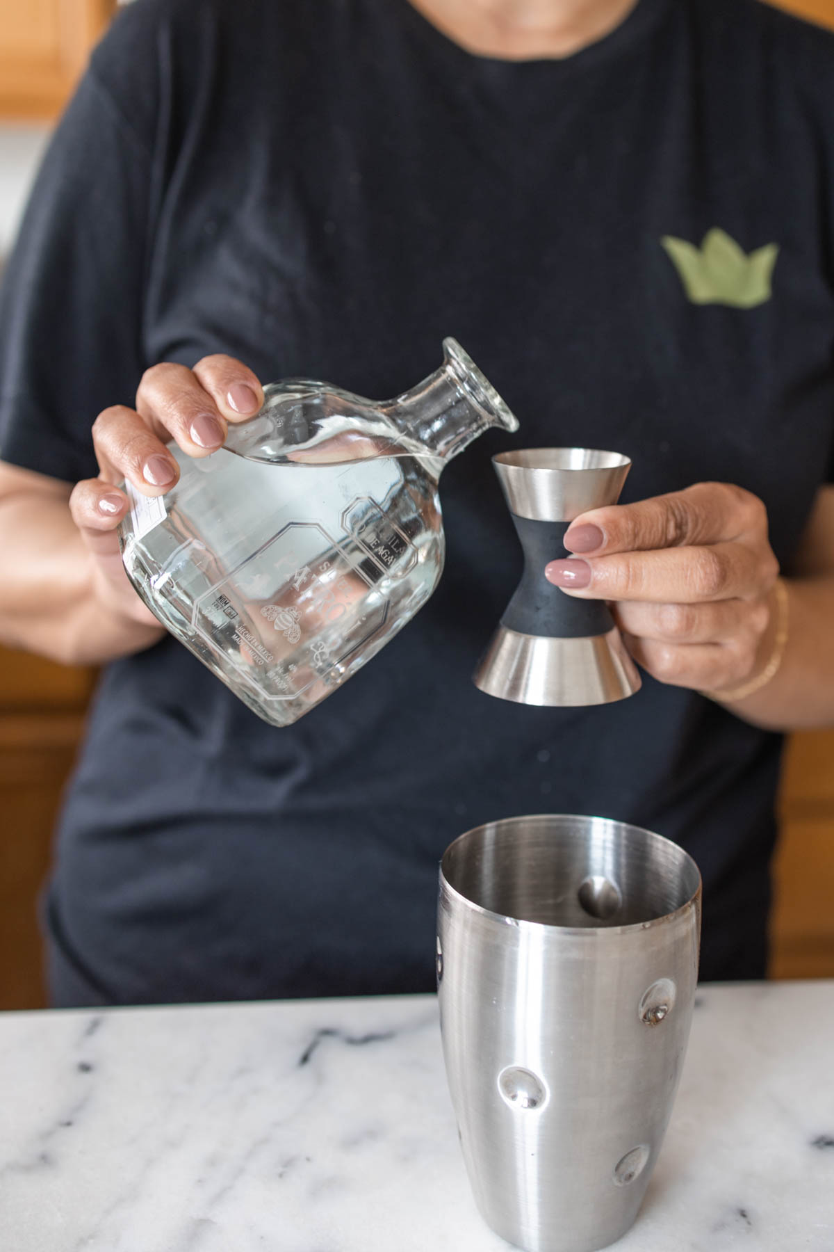 A person about to pour some Patron Silver tequila into a jigger on top of a cocktail shaker.