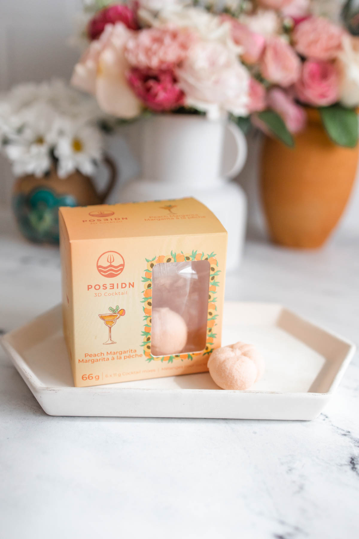 A pretty peach-colored box of Poseidn Peach Margarita Cocktail Bombs on a small hexagon white plate.