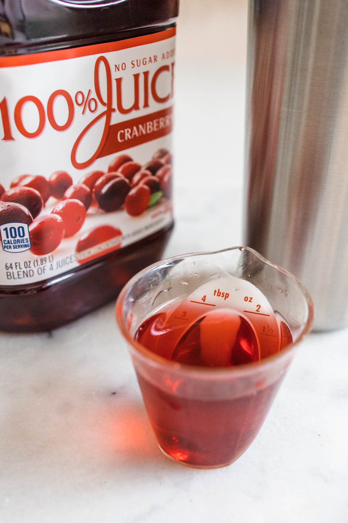 Cranberry juice inside a measuring cup in front of a cranberry juice bottle.