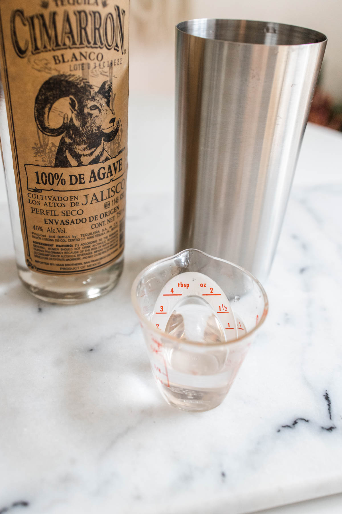 A Cimarron Blanco tequila bottle beside a cocktail shaker and a small measuring cup.