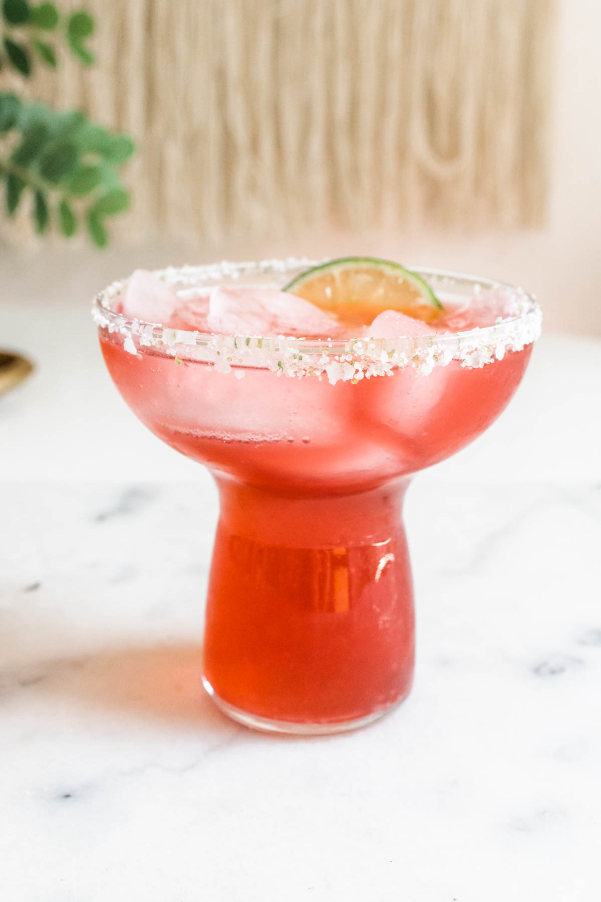 A glass of cranberry margarita with a  salt rim, fresh ice, and a lime slice garnish.