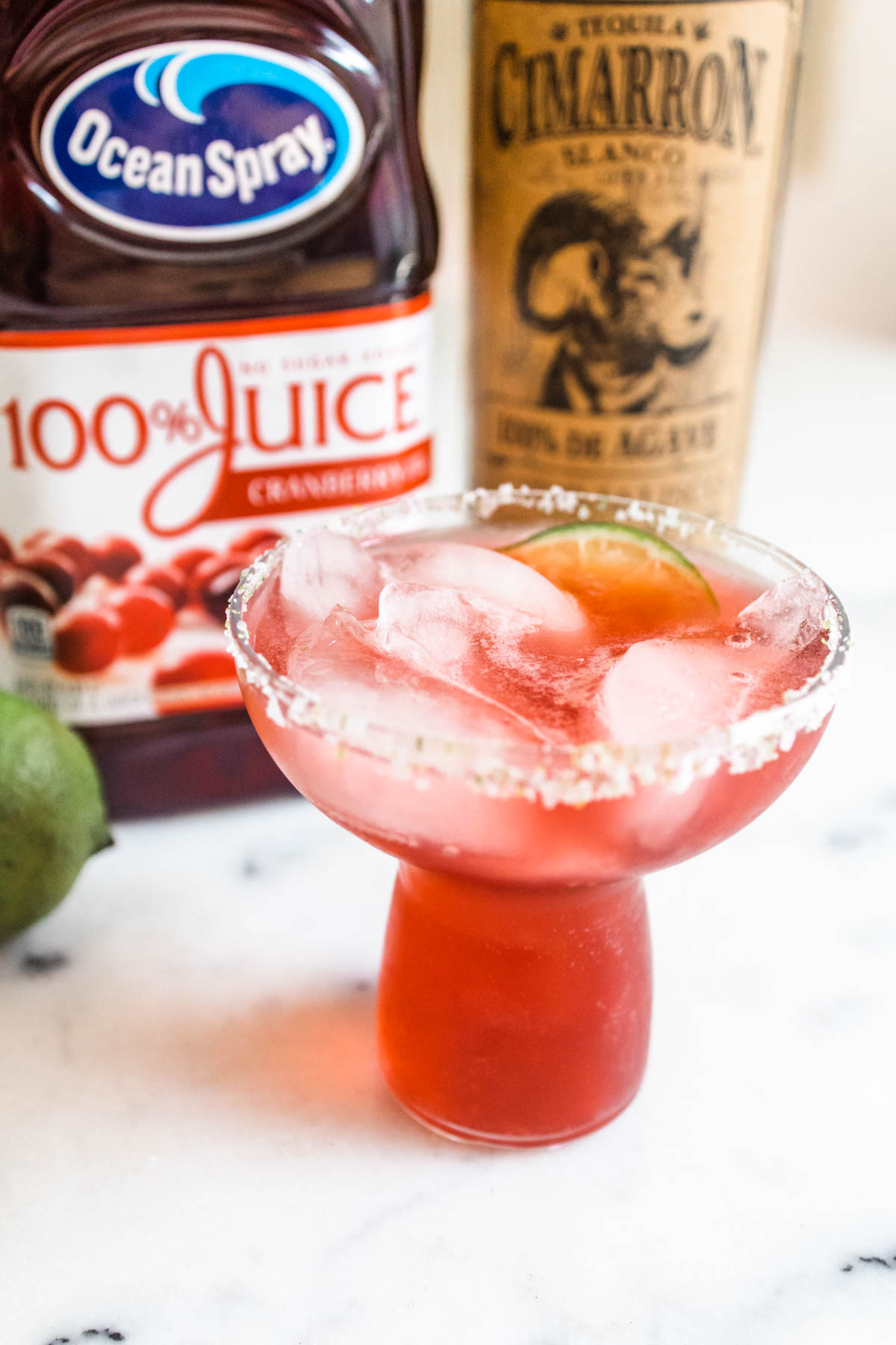 A beautifully red easy cranberry margarita with ice in a glass with a salted rim. 