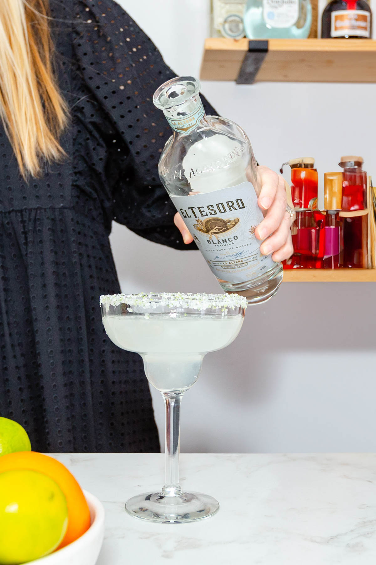 Woman pouring tequila into a margarita in a glass.