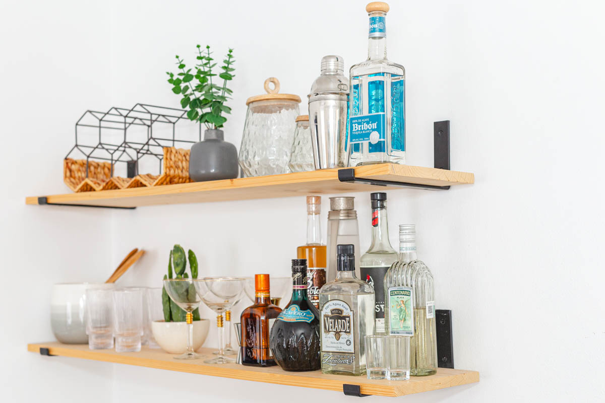 Bottles of tequila on a wall shelf next to glasses and a cactus.